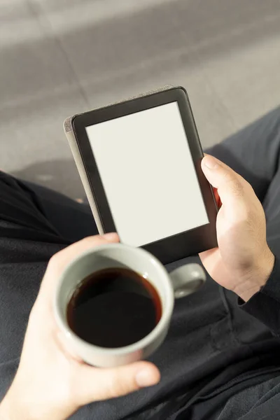 Tanınmayan bir çocuğun elektronik kitap okuması ve elinde bir fincan kahveyle koltukta oturması rahatlatıcı..