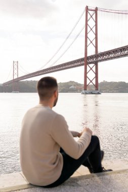 Tanımlanamayan genç adam 25 Nisan köprüsüne bakarken sırtı dönük bir şekilde yerde oturuyor..