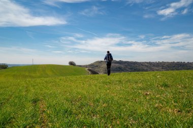 Doğanın ortasında yeşil bir çayırda sırt çantasıyla yürüyen tanınmayan genç bir adam. Spor ve kendini geliştirme kavramı.