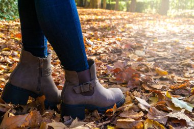 Tanımlanamayan kadın botları sonbahar arka planında kuru yapraklarla ön planda