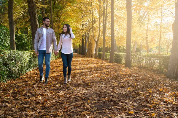 Sonbaharda parkta el ele yürüyen genç bir çift.