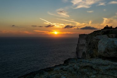 Ön planda kayalıklar, arka planda deniz, gün batımında renkli ve güzel bir gökyüzü..