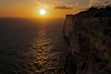 Kayalıklardan denizin üzerinde gün batımının fotoğrafı.