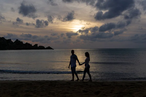 Young couple in love walking on the shore of the beach with the sunset in the background.