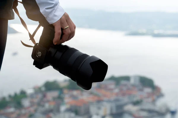 Detail of the hand of an unrecognizable girl holding her camera with a view of the fjord in the background in Norway.