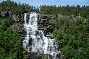 Large waterfall that rises in the mountains surrounded by green trees in Norway