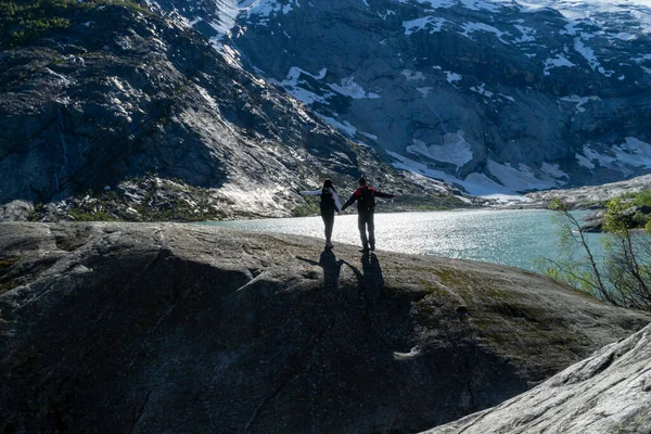 Unrecognizable couple of backpackers on top of a rock with the glacier river in the background with their arms raised.