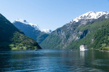 Geirangerfjord landscape with a cruise ship and snow-capped mountains in the background.