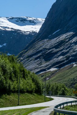 Landscape of a road in the foreground with snow-capped mountains in the background.