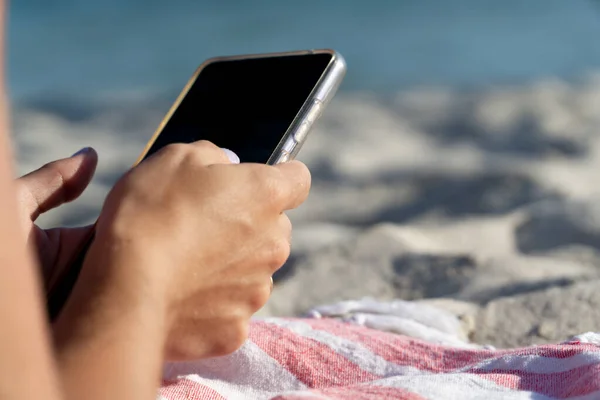 Detail of the hands of a woman with painted nails holding her smartphone on the beach
