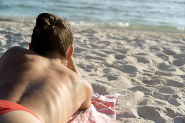 Unrecognizable woman sunbathing lying on a towel in the sand on the beach on a summer day with plenty of copy space