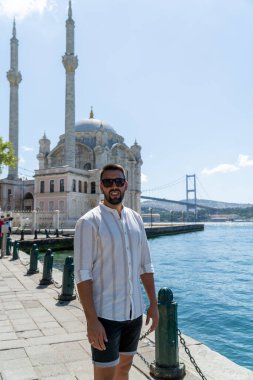 Sakallı ve güneş gözlüklü bir gencin portresi ortakoy camisinin ve İstanbul 'un ünlü köprüsünün önünde poz veriyor..