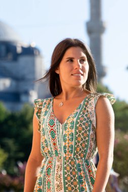 Ön planda genç bir kadın ve arka planda mavi cami gün batımında..