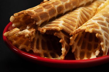 Wafer siyah arka planda kırmızı bir tabakta yuvarlanıyor. Siyah arkaplanda çay için tatlı