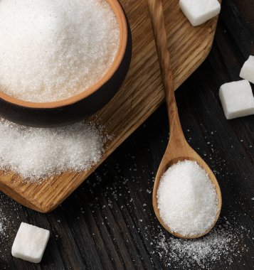 Tahta kaşık ve fincanda siyah desenli ahşap arka planda beyaz granüle şeker.