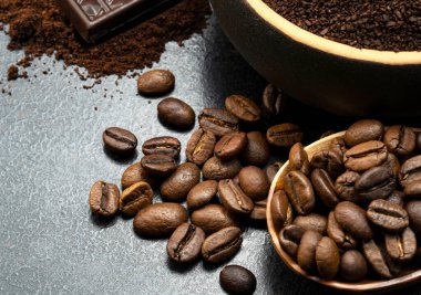 bir kaşık dolusu kahve çekirdeği ve siyah arka planda bir kalıp koyu çikolatalı kahve.