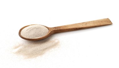 Beyaz arka planda izole edilmiş ahşap kepçeyle kuru maya.