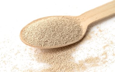 Beyaz arka planda izole edilmiş ahşap kepçeyle kuru maya.