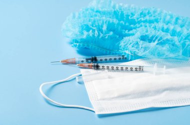 Mavi arka planda, şırıngalı ve tıbbi kapaklı bakteri ve virüslerden kalma tek kullanımlık tıbbi maske. Koronavirüsün yayılmasını durdur, nefsi müdafaa..