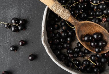 Siyah arka planda, kaşıkla bir kasede siyah frenk üzümü.