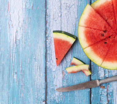 Kesilmiş karpuz ve mavi ahşap arka planda bir bıçak..