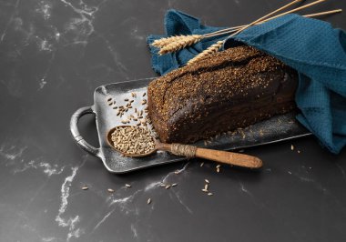 Tüm ev yapımı siyah ekmek mermer bir masada mısır gevreği ve demir tepside bir kaşık.