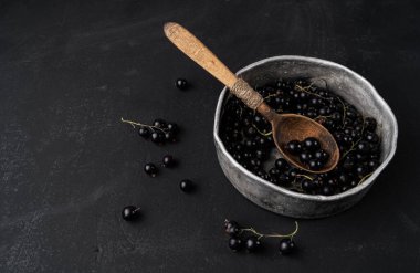 Siyah arka planda, kaşıkla bir kasede siyah frenk üzümü.