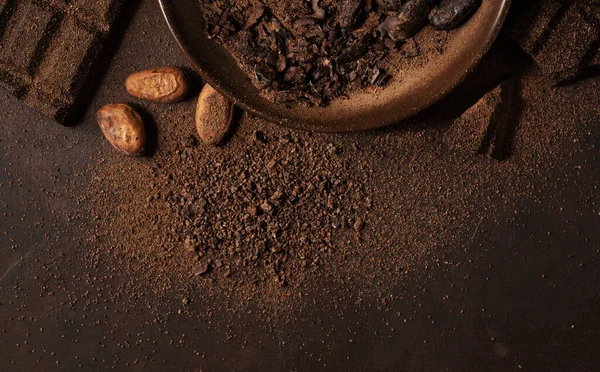 チョコレートとカカオのコンセプト ココア豆の近くのボウルにココアパウダーと黒の背景に壊れたチョコレート — ストック写真