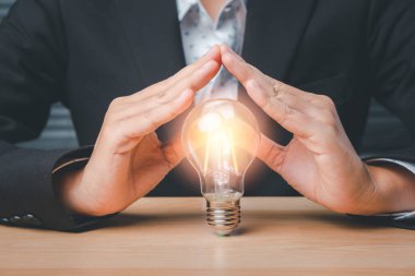 Light blub under hands in gesture of protection on wooden desk, new ideas of business, innovative technology network connection.	