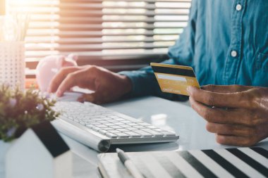 Kredi kartı tutan ve dizüstü bilgisayar kullanan bir adam. Çevrimiçi alışveriş, İşadamı veya girişimci çalışma, e-ticaret, internet bankacılığı, harcama, ev kavramından çalışma