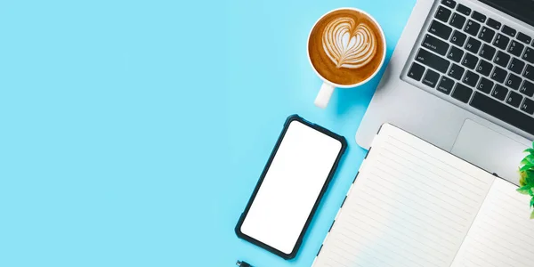 写字台配备笔记本电脑 空白屏幕智能手机 一杯咖啡 蓝色背景笔记本 带复制空间的顶部视图 — 图库照片