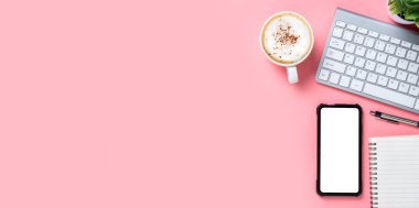 Klavye bilgisayarlı ofis masası, boş ekran akıllı telefon, bir fincan kahve, pembe arka planda kalem, not defteri, fotokopi alanı olan üst görünüm,.