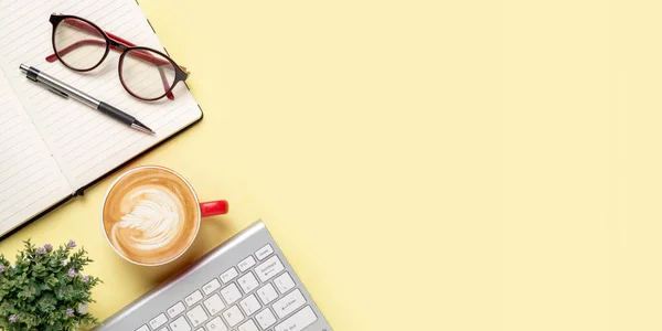 Office desk with keyboard computer, Pen, eyeglass, notebook, Cup of coffee on yellow background, Top view with copy space, Mock up.