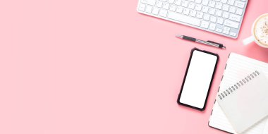 Bilgisayarlı ofis masası, boş ekran akıllı telefon, not defteri, kalem, pembe arka planda bir fincan kahve, fotokopi alanı olan üst görünüm,.