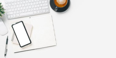 Top view, White office desk with keyboard, Blank screen smart phone, Notebook, pen and Cup of coffee, copy space, Mock up.	