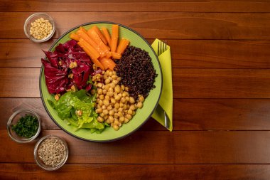 Buda kasesi ahşap masada. Vejetaryen yemeği. Akdeniz diyeti. Sağlıklı beslen. Yaz yemekleri. Renkli yemekler. Bir tabak nohut, siyah pirinç, havuç, kırmızı salata ve marul. Düz yatıyordu. Boşluğu kopyala.