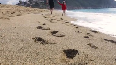 Sahilde kumsalda yürürken kızın ve babanın el ele tutuşması.