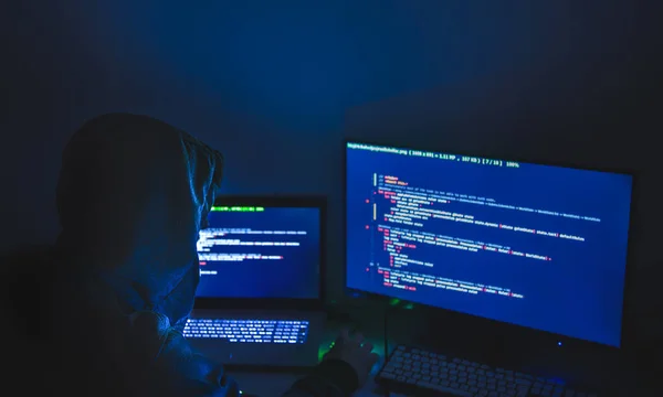 Datorhackare silhuett av huva, man använder laptop och övervaka för att stjäla data. Begreppet it-brottslighet. — Stockfoto