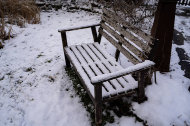 Old bench covered in snow and standing in grass