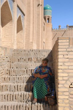 Yaşlı bir kadın gölgede oturuyor, merdivenlerde. Özbekistan
