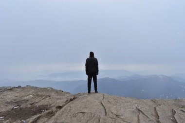 Sırt çantalı genç adam dağın tepesinde. Bir adam dağın yamacında huzur içinde duruyor..