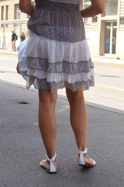 legs of a young lady on the asphalt in action, short summer dress, white sandals