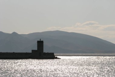 Deniz feneri, deniz feneri ve yakındaki adanın tepelerine doğru bakın. Güneş ışınları deniz yüzeyinden yansıyor.
