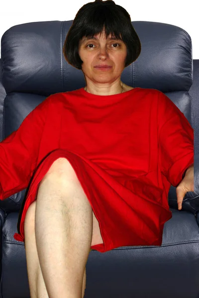 赤いドレスの美しい女性が座っていますアームチェアで彼女の裸の足が交差 — ストック写真