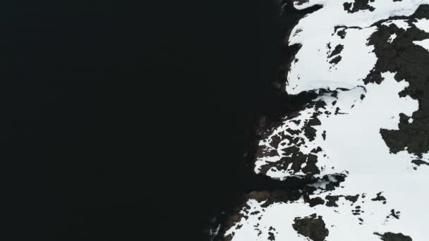 Dron létá v černých vodách oceánu, které omývají skalnaté pobřeží Skandinávie nebo Severní Ameriky. Arktický oceán, skály pokryté sněhem. Snowy Grónsko — Stock video
