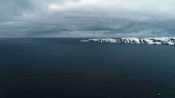 Повітряний постріл у Північний Льодовитий океан у погану пагоду з сірими хмарами, які несуть шторм біля скелястого берега, вкритого снігом. Жорсткий клімат півострова Кола. Погана погода в морі — стокове відео