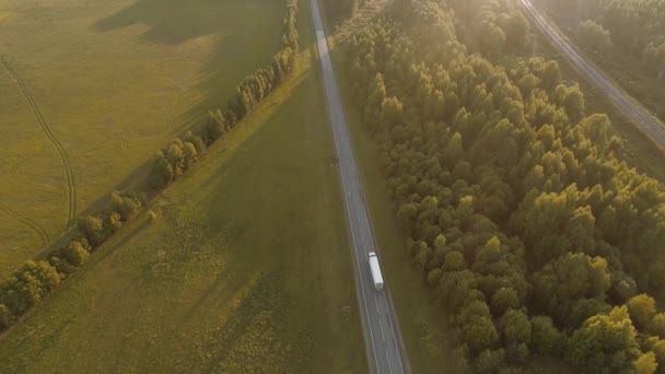 En un brillante día de verano, un dron vuela sobre la carretera a lo largo de la cual los coches y camiones con remolques se mueven en el arroyo, transportando sus mercancías a través del país. Entrega de mercancías a cualquier distancia — Vídeos de Stock