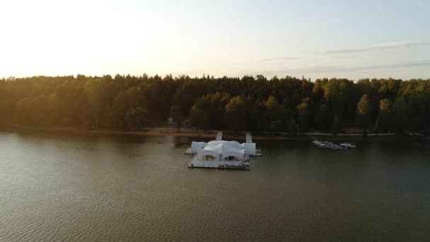 Το drone πετάει μέχρι την προβλήτα στην οποία υπάρχει μια μεγάλη λευκή μαρκίζα στην οποία γίνονται πάρτι και βραδινές εκδηλώσεις. Στην όχθη του ποταμού υπάρχει ένα ψηλό δάσος. Δεξαμενή νερού Istra — Αρχείο Βίντεο