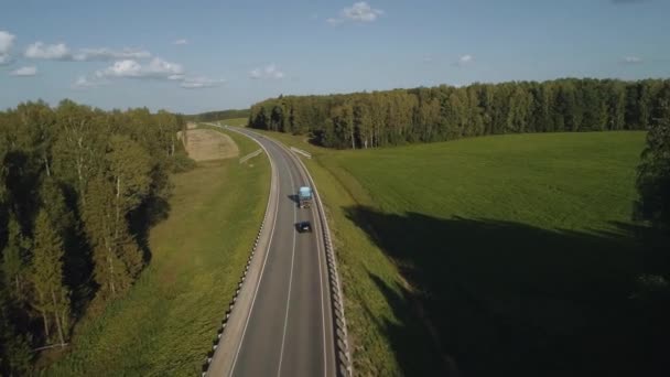 A drón egy autót és egy teherautót követ egy út mentén, ahol autók közlekednek a patakban. A szállítási logisztika és a jó utak az állam egészséges gazdaságának jelei. Gyorsforgalmi út egy nyári napon Videóklipek