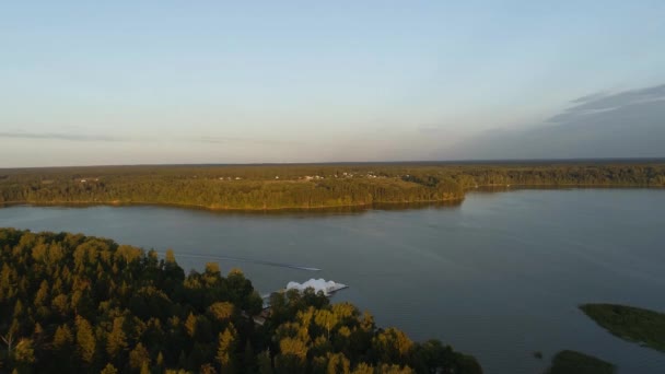 Piękny widok z drona zbiornika Istra, Dron leci nad lasami i jeziorem, wzdłuż którego pędzi motorówka, na brzegu znajduje się piękny biały markiz dla imprez Wideo Stockowe